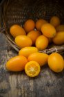 Basket of fresh kumquats on dark wood — Stock Photo