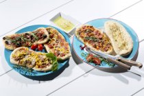 Pizzas with ham, salami, mozzarella, tomato, arugula, maize and olives on white wood — Stock Photo
