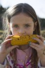 Portrait of little girl eating grilled corn cob — Stock Photo