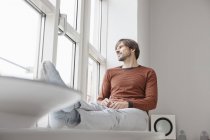 Man sitting on window sill and looking out of window — Stock Photo