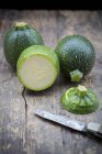 Sliced and whole round courgettes and knife on dark wooden table — Stock Photo