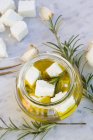 Glass of diced sheep cheese pickled in olive oil and rosemary on white marble — Stock Photo