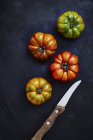 Four beef tomatoes and knife on black surface — Stock Photo