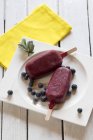 Plate of two wild-berry ice lollies on white wooden table, elevated view — Stock Photo
