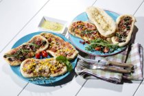 Pizzas with ham, salami, mozzarella, tomato, arugula, maize and olives on white wood — Stock Photo