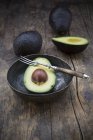 Halbierte und ganze Avocados mit Schüssel und Gabel auf Holztisch — Stockfoto