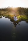 Austria, Contea di Salisburgo, Giovane donna seduta vicino al lago di montagna e che fa meditazione — Foto stock
