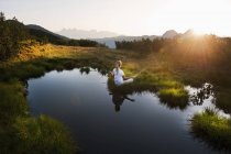 Austria, Contea di Salisburgo, Giovane donna seduta vicino al lago di montagna e che fa meditazione — Foto stock