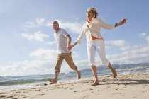 Senior couple running along beach, smiling — Stock Photo