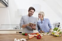 Ältere Paare bereiten Essen zu, während sie digitale Tablets suchen — Stockfoto