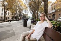 Spain, Mallorca, Palma, Young woman sitting on bench, smiling, portrait — Stock Photo