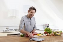 Mann bereitet Essen zu, während er digitales Tablet sucht — Stockfoto