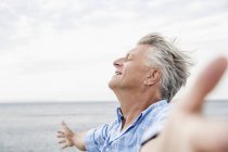 Senior steht mit ausgestreckten Armen am Strand — Stockfoto