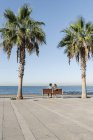 Metà coppia adulta seduta sulla panchina sotto le palme al mare — Foto stock