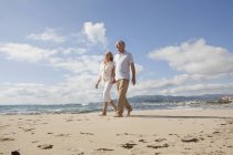 Senior couple walking along beach, smiling — Stock Photo