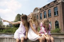 Tre ragazze sedute su un muro a guardare qualcosa — Foto stock