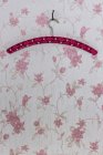 Cintre à vêtements fixé avec un clou plié accroché sur papier peint avec motif floral rose — Photo de stock