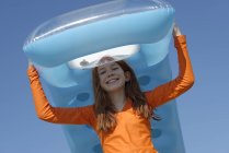 Portrait of smiling girl carrying air mattress on her head wearing sun protection longsleeve — Stock Photo