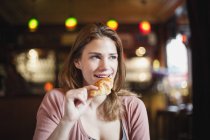Francia, París, retrato de una joven feliz comiendo un croissant en un café - foto de stock