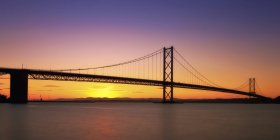 UK, Scotland, View of Forth Bridge at sea against sun at dawn — Stock Photo