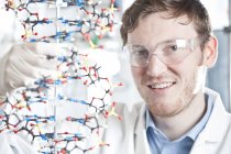 Portrait rapproché de jeune scientifique avec modèle ADN, souriant au laboratoire — Photo de stock
