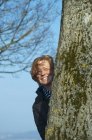 Femme mûre se cachant derrière l'arbre, souriant — Photo de stock