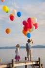 Ragazzo e ragazza in piedi sul molo con palloncini volanti al lago Starnberg — Foto stock
