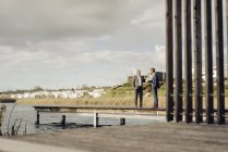 Two businessmen standing on jetty at lake and talking — Stock Photo