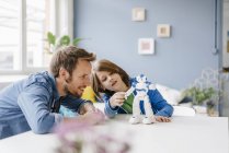 Счастливые отец и сын играют с роботом на столе дома — стоковое фото