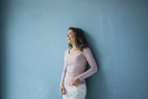 Laughing woman leaning against blue wall — Stock Photo