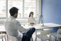 Mann sitzt Frau gegenüber und benutzt Computer im Büro — Stockfoto