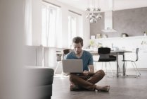 Uomo seduto sul pavimento in un loft e che lavora su un computer portatile — Foto stock
