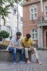 Due amici multiculturali che condividono il cellulare in città — Foto stock
