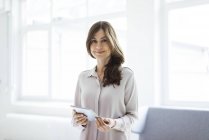 Portrait of smiling woman standing in bright room and holding tablet — Stock Photo
