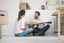 Coppia seduta sul pavimento in nuova casa e suonare la chitarra — Foto stock