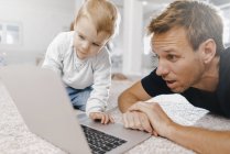 Incroyable père avec petite fille en utilisant un ordinateur portable sur le sol — Photo de stock