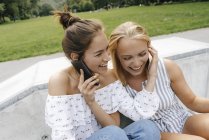 Due giovani donne felici con i telefoni cellulari seduti in uno skatepark — Foto stock