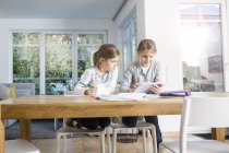 Deux filles faisant leurs devoirs à table ensemble à l'aide d'une tablette — Photo de stock