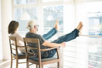 Entspanntes älteres Paar sitzt auf Stühlen zu Hause mit den Füßen nach oben — Stockfoto