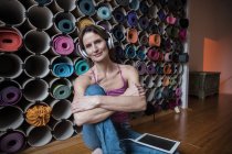 Retrato de mujer madura sonriente escuchando música frente a surtido de esterillas de yoga - foto de stock