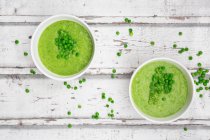 Two bowls of pea soup and peas on woodedn background — Stock Photo