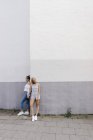 Дві молоді жінки, що стоять біля кута будівлі, тримаючись за руки — стокове фото