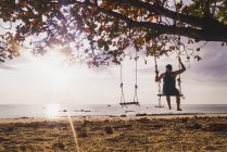 Tailândia, Phi Phi Islands, Ko Phi Phi, homem em árvore balançando na praia ao pôr do sol — Fotografia de Stock