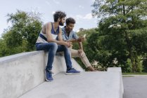 Dois amigos multiculturais compartilhando celular no skatepark — Fotografia de Stock