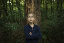 Portrait of confident girl standing at tree trunk in forest — Stock Photo