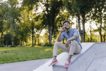 Sonriendo joven afroamericano hombre hablando por teléfono celular mientras está sentado en skatepark - foto de stock