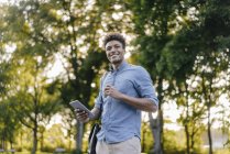 Sorrindo jovem afro-americano segurando celular no parque — Fotografia de Stock