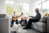 Duas meninas no sofá tocando guitarra com avô e cachorro — Fotografia de Stock