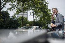 Souriant jeune homme d'affaires avec café pour aller au téléphone — Photo de stock