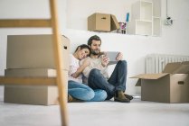 Couple assis dans une nouvelle maison entourée de boîtes en carton et regardant la tablette — Photo de stock